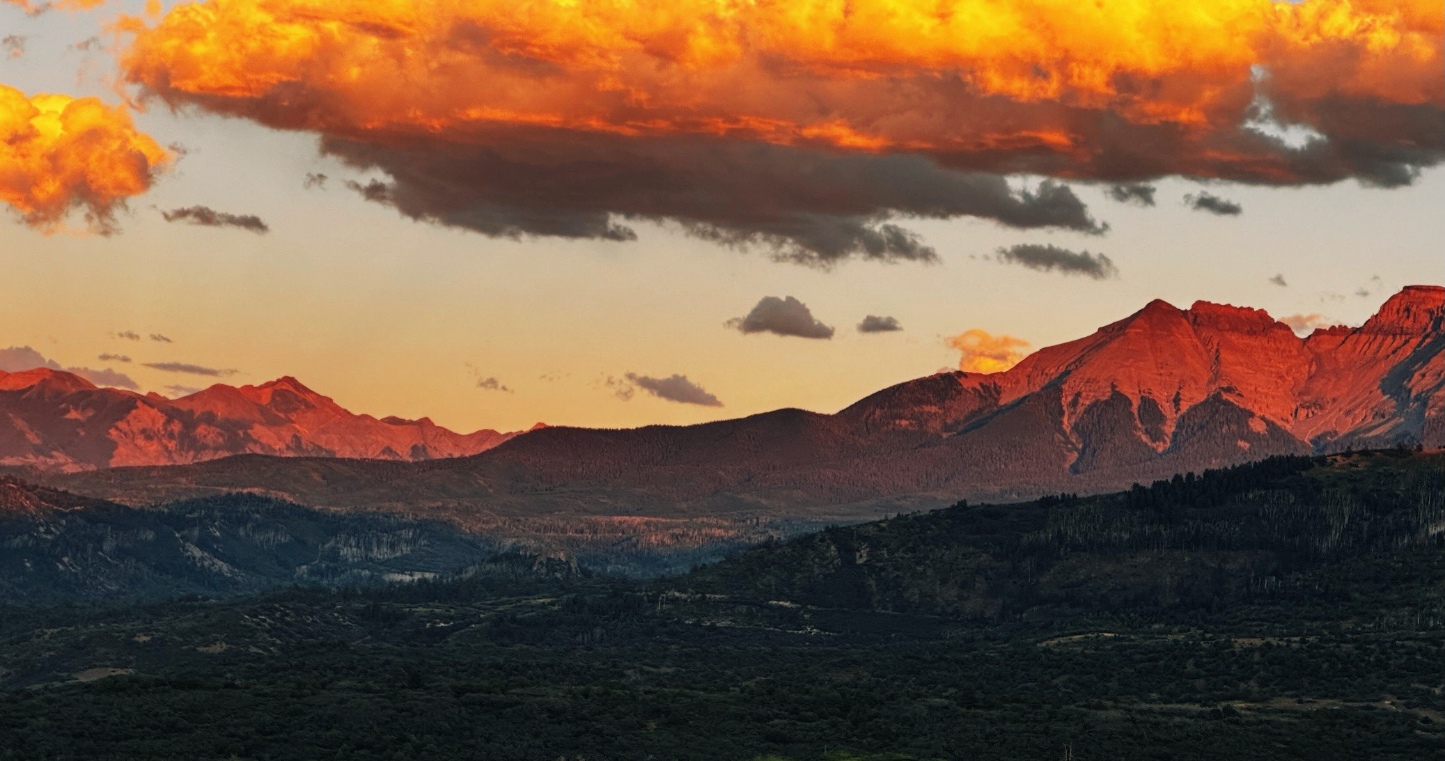 Warm sunset light catches a mountain ridgeline beneath a brilliant orange sky, photographed by Cheslee Klinger.