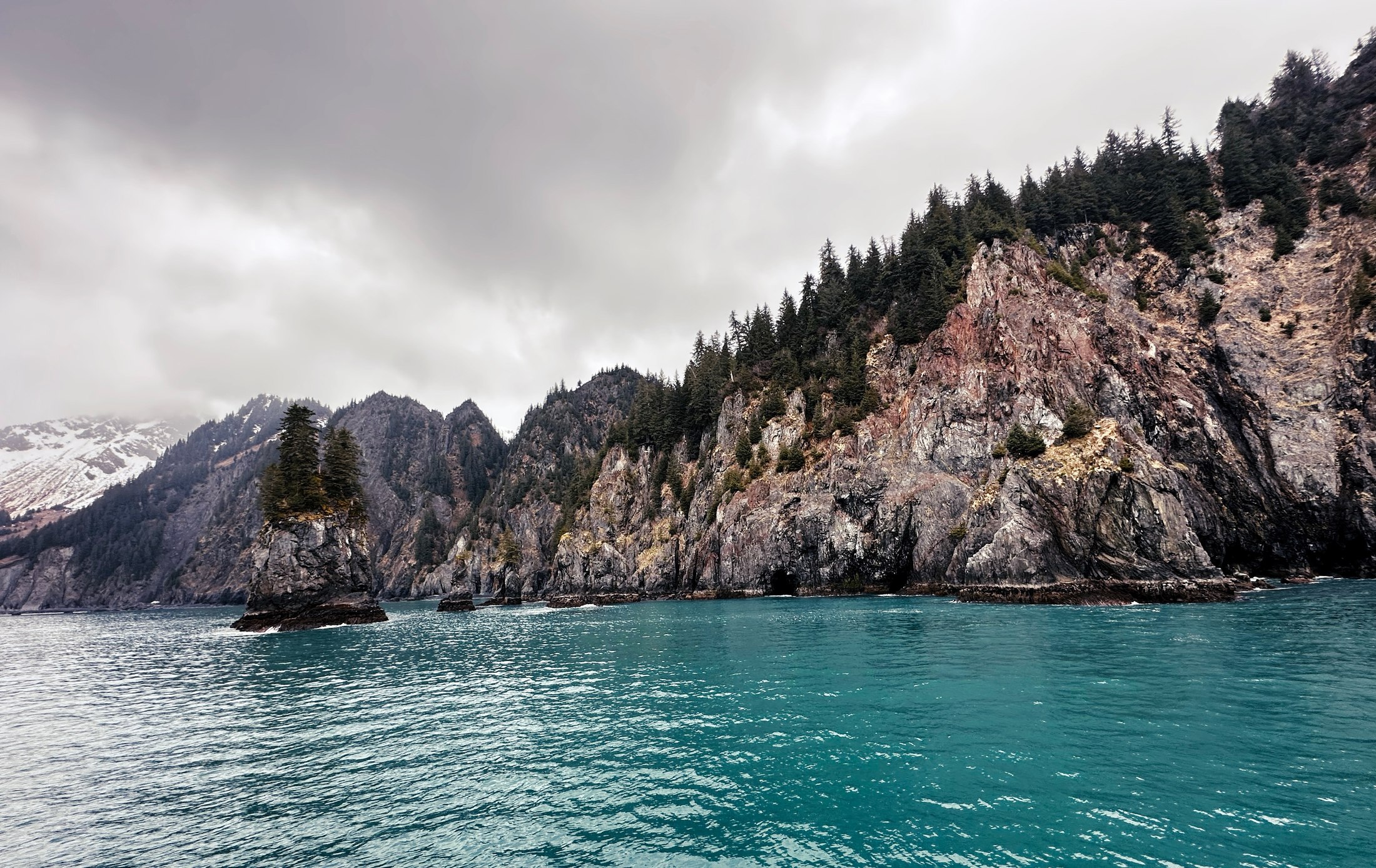 Turquoise water beneath a rugged, forested coastline.