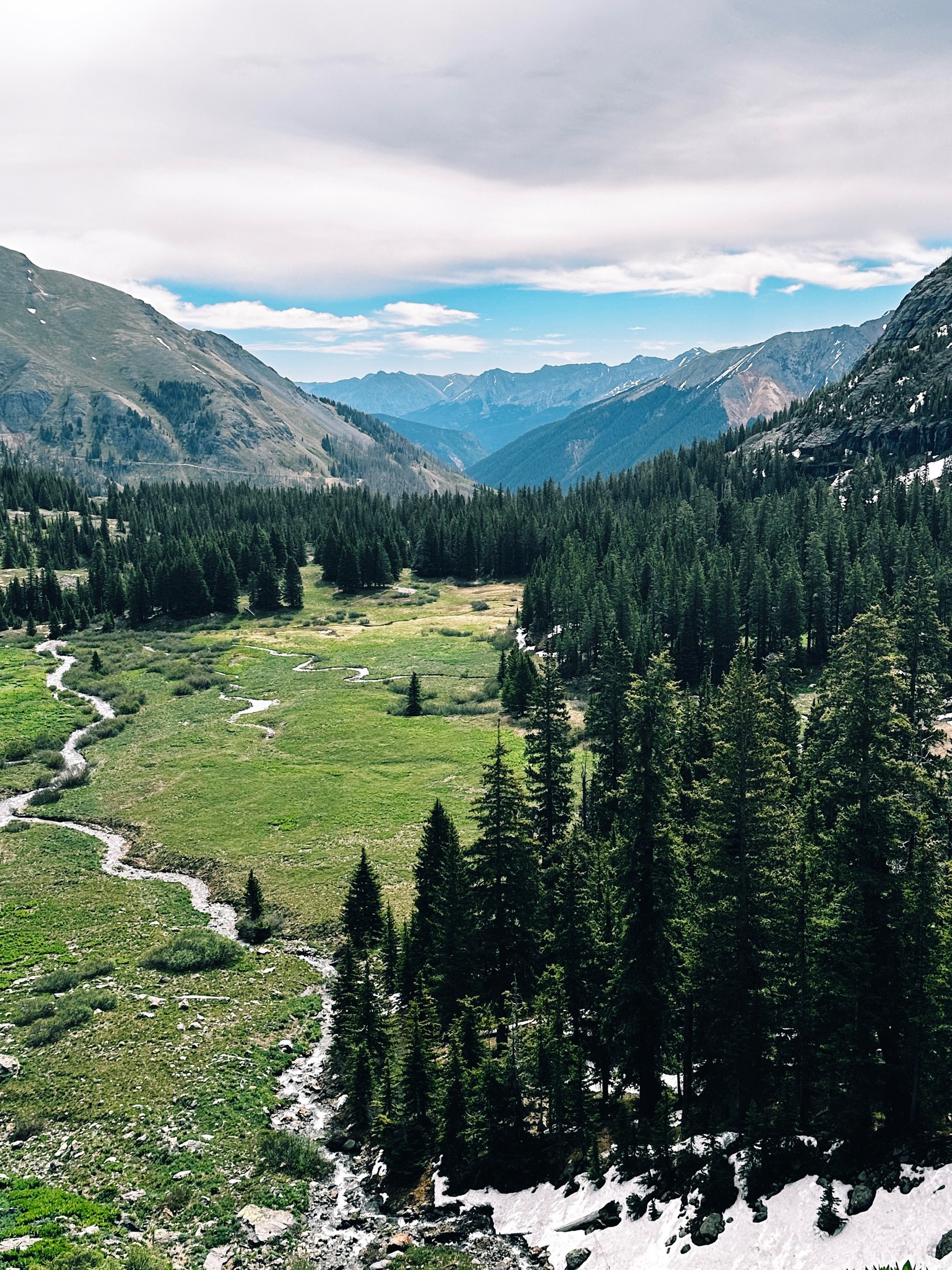 A stream winds through a green alpine valley surrounded by mountains.